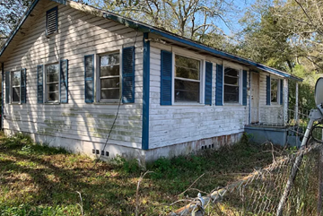 Jacksonville house for rent - A white house with blue trim and windows is surrounded by grass and trees.