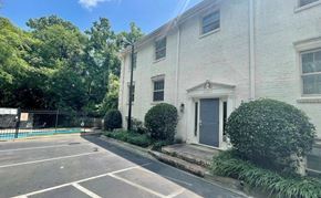 Charlotte house for rent - A white building with a grey door and windows is surrounded by greenery.