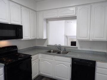 Dallas apartment for rent - A kitchen with white cabinets and black appliances.