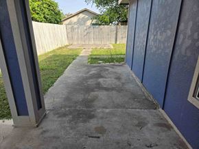 Brownsville house for rent - A concrete walkway leads to a backyard with a wooden fence.