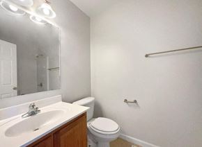 Winston-Salem house for rent - A white bathroom with a toilet, sink, mirror, and light fixture.