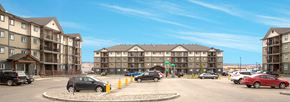 Dawson Creek apartment for rent - A parking lot with cars and apartment buildings in the background.