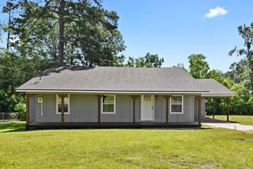 Leesville house for rent - A small house with a grey roof and white trim is surrounded by green grass and trees.