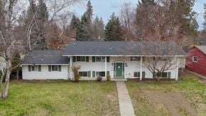 Spokane house for rent - A white house with a green door is surrounded by trees.