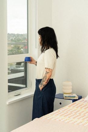 Victoria apartment for rent - A woman with a tattoo on her arm is standing by a window holding a blue cup.