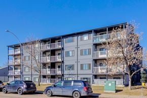 Edmonton apartment for rent - Two cars are parked in front of a grey apartment building.
