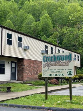 Matewan apartment for rent - A building with a sign that says "Creekwood Apartments" in front of a forest.
