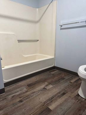Wheeling apartment for rent - A white toilet sits in a bathroom with wood flooring and white walls.
