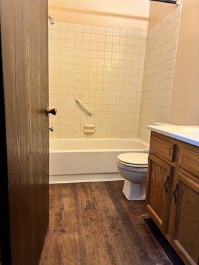 Coldwater apartment for rent - A white toilet sits in a bathroom with a wooden floor and a white tiled shower.