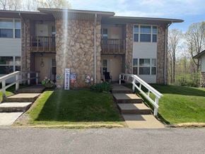 Spencer apartment for rent - A sunny day at a stone building with a white fence and a small garden in front.