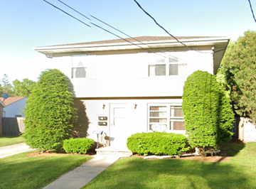 Oshkosh apartment for rent - A white house with a grey roof and a grey door is surrounded by green bushes.