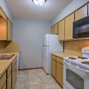 Omaha apartment for rent - A kitchen with a white refrigerator, a stove, and wooden cabinets.
