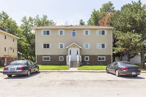 Ashland apartment for rent - A two-story building with a beige facade and a white door is surrounded by trees and has two cars parked in front.