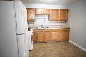 Omaha apartment for rent - A kitchen with a white refrigerator, wooden cabinets, and a tiled backsplash.