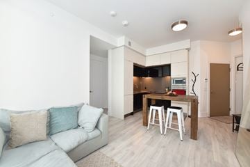Toronto apartment for rent - A living room with a grey couch and a kitchen area in the background.