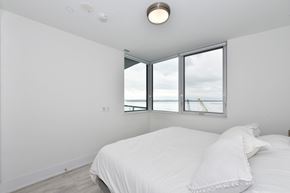 Toronto apartment for rent - A white bedroom with a large bed and a window overlooking the beach.