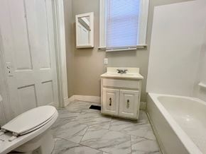 Louisville house for rent - A white toilet sits in a bathroom with a marble floor and a white bathtub.