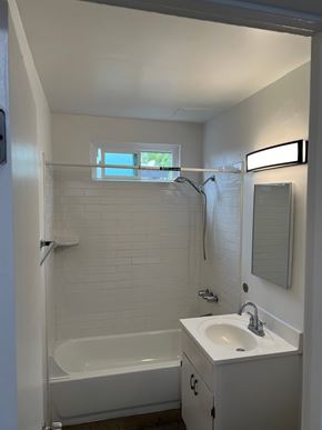 Cudahy apartment for rent - A white bathroom with a tub, sink, mirror, and a window.