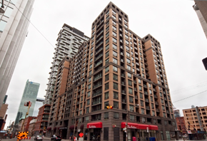 Toronto apartment for rent - A large brown building with many windows is in the middle of a city street.