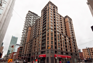 Toronto apartment for rent - A large brown building with many windows is in the middle of a city street.
