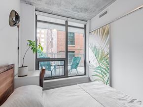 Toronto apartment for rent - A bedroom with a large bed and a view of a balcony with chairs.