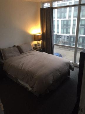 Toronto apartment for rent - A bed with a grey comforter and pillows in a room with a window.