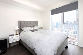Toronto apartment for rent - A bedroom with a large bed and a city view through the window.