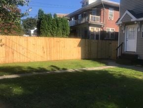 West Lawn house for rent - A wooden fence separates a green lawn from a house.