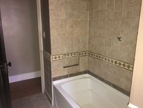 West Lawn house for rent - A white bathtub sits in a bathroom with beige tiles.