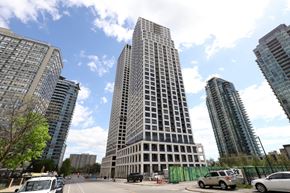 Mississauga apartment for rent - A tall building stands in front of other buildings and trees.