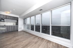 Toronto apartment for rent - A spacious room with wooden floors and large windows overlooking a cityscape.