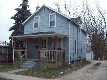 Lansing house for rent - A blue house with a porch and a dirt road in front.