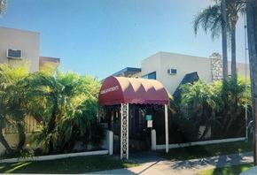 Anaheim apartment for rent - A building with a red awning is surrounded by palm trees.