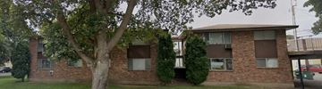 Spokane apartment for rent - A tree in front of a brick building with a green bush to the right.