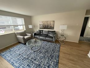 Denver apartment for rent - A living room with a grey couch, a glass table, and a blue rug.