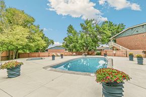 Lakewood apartment for rent - A pool surrounded by trees and concrete planters with flowers.