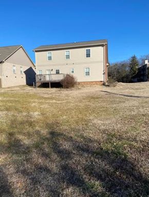 Nashville house for rent - A large, two-story building with a balcony is situated in a grassy area with a smaller building to its left.