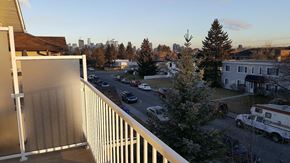 Calgary apartment for rent - A view from a balcony overlooking a parking lot and trees.