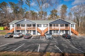 Winston-Salem apartment for rent - A parking lot with cars and a two-story building with a green roof.