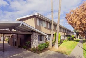 San Jose apartment for rent - A building with a brown and beige exterior is surrounded by trees and a stone pillar.