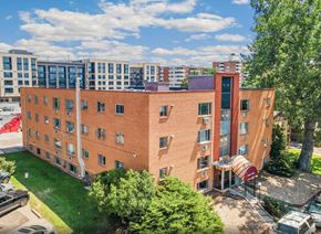 Denver apartment for rent - A red brick building with a red awning sits in front of a parking lot.