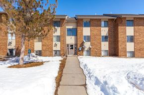 Craig apartment for rent - A snow-covered walkway leads to a brick apartment building with a green sign on the left.