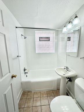 Denver apartment for rent - A white toilet is in a bathroom with a white tub and sink.