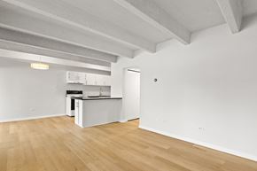 Denver apartment for rent - A kitchen with white cabinets and a white fridge is in a room with wooden floors and white walls.