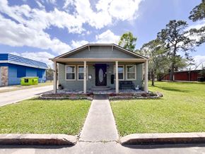 Bay City house for rent - A small house with a grey roof and a blue door is surrounded by a grassy lawn.