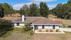 Weirsdale house for rent - A house with a red roof and a chimney is surrounded by trees.
