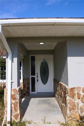 Weirsdale house for rent - A white door with a glass window is set in a white wall with a stone pillar on each side.