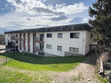 Fort St James apartment for rent - A white building with a black roof and a green lawn in front.
