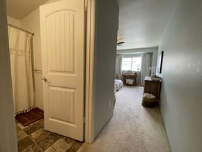 Kapolei apartment for rent - A hallway with a carpeted floor, a door on the left, and a bedroom with a bed and a dresser on the right.