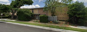 Dallas apartment for rent - A brown building with a black fence and a tree in front.